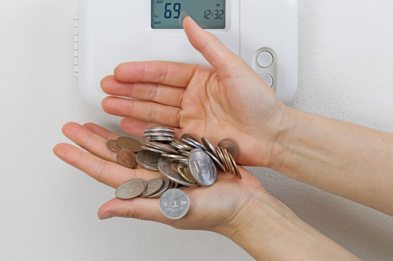 Homeowner holding tons of change in front of thermostat of their Leominster home.