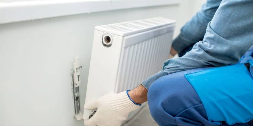 Workman mounting water heating radiator on the white wall indoors, close-up view