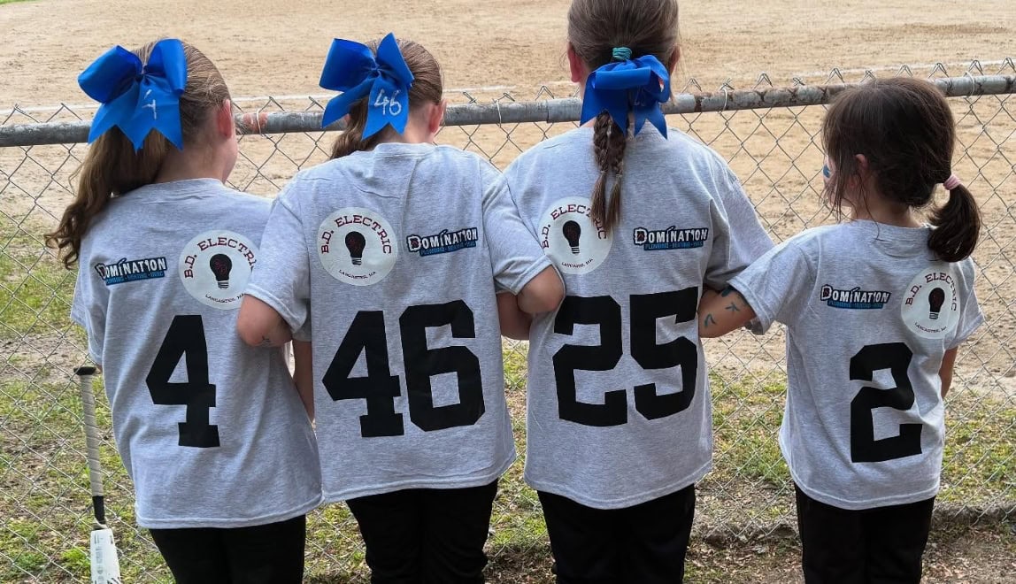 Girl softball players from the Leominster Lassie League standing along fence at local fields.