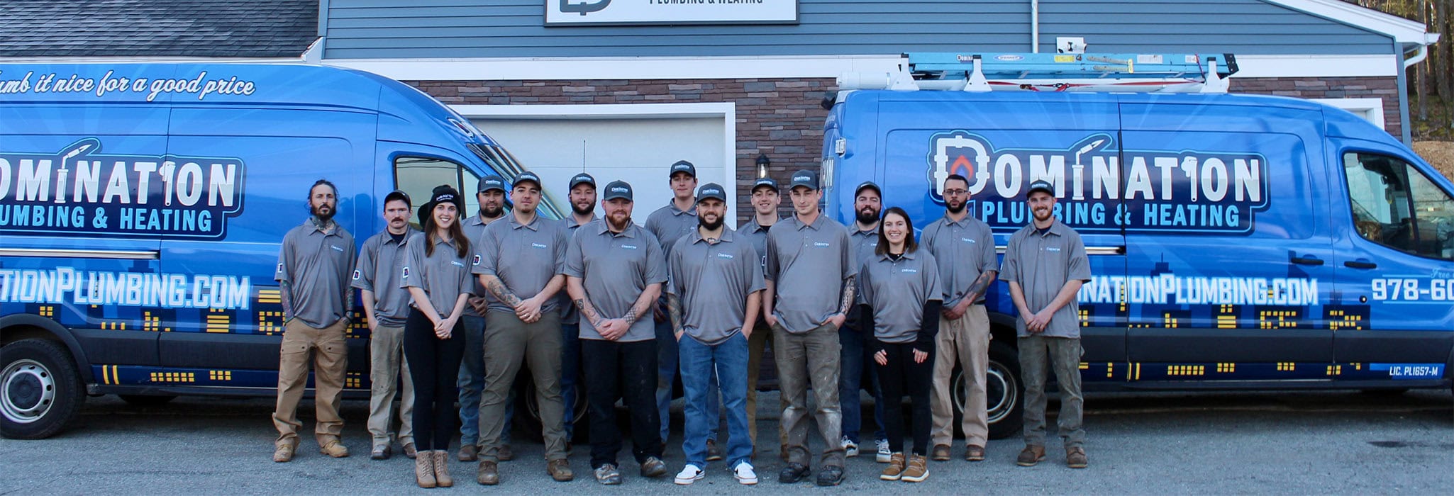 The Domination Plumbing and Heating team is standing outside their office with two service trucks.