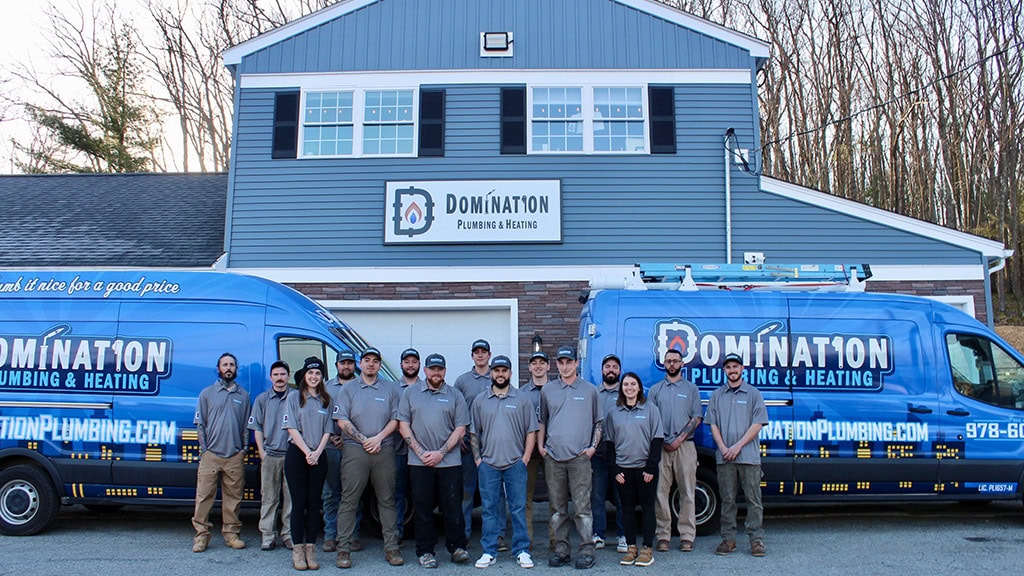 The Domination Plumbing and Heating team standing outside their office and two service trucks.